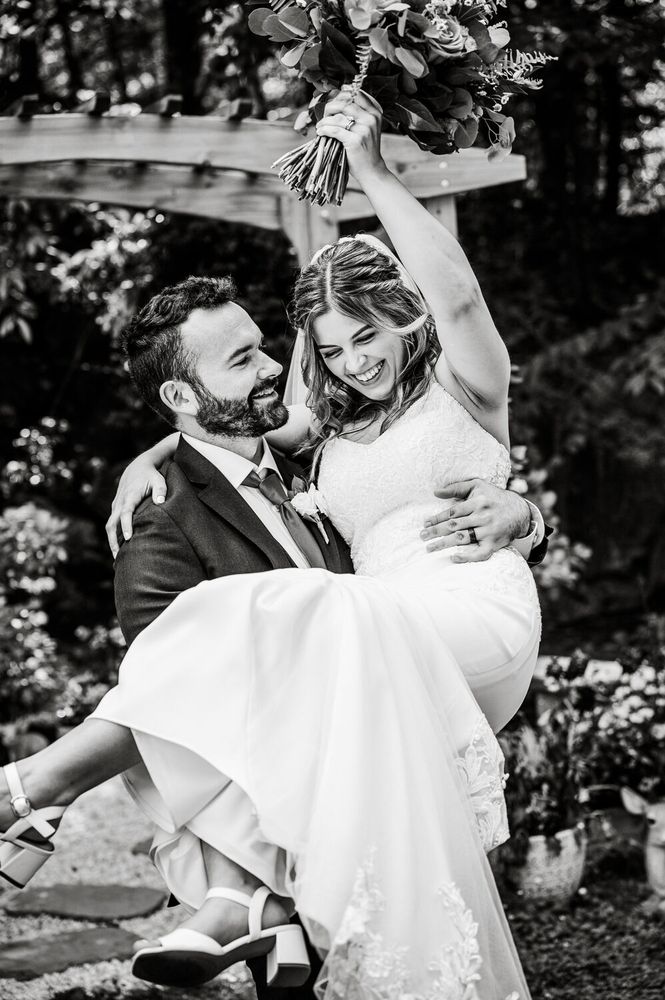 A groom carrying his laughing bride as she raises her bouquet
