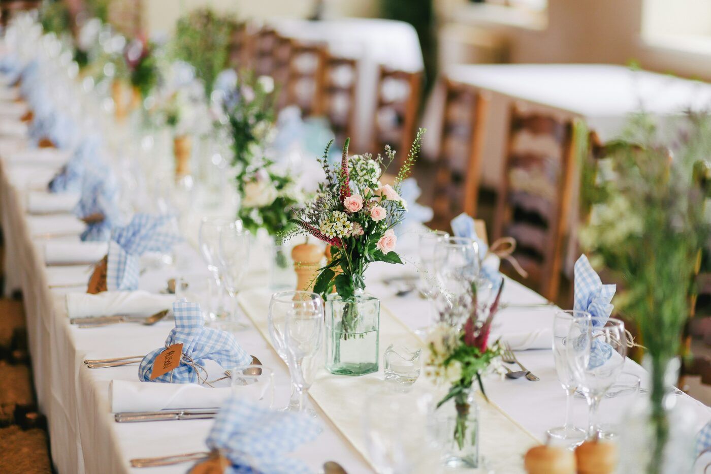 A long reception table set with gingham napkins and wildflower centerpieces